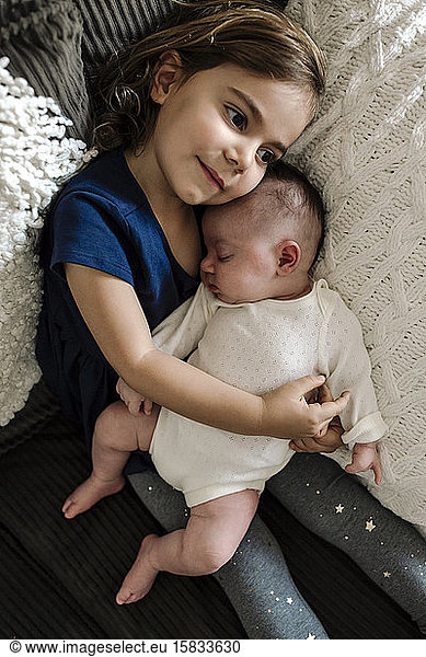 Dreamy big sister snuggling sleeping newborn with everyday disability