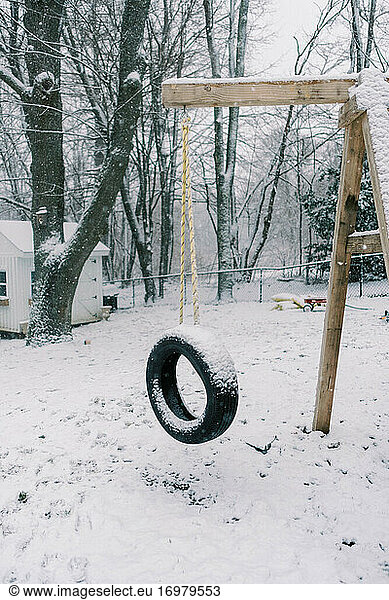 dreary dark wintery backyard swing with tire covered in fresh snow