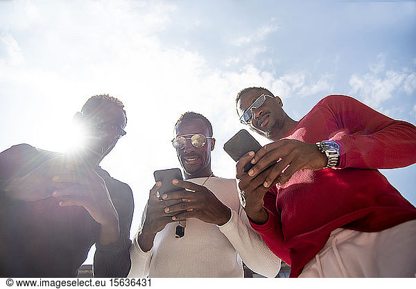 Drei coole junge Männer mit Mobiltelefonen im Gegenlicht
