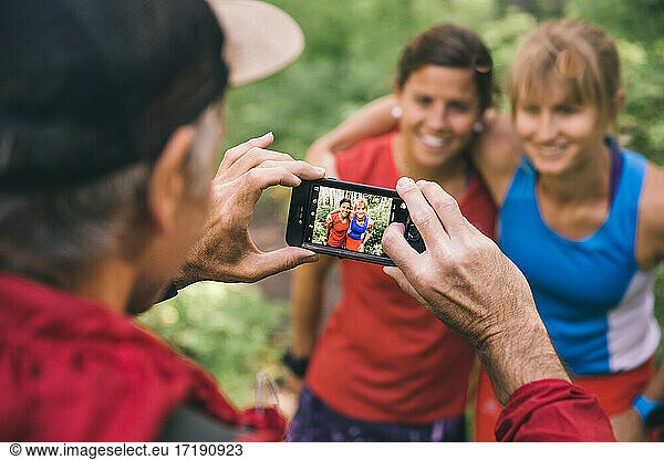 Drei Freunde laufen zusammen und halten an  um ein Foto mit dem Smartphone zu machen