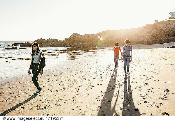 Drei Geschwister gehen bei Ebbe und Sonnenuntergang am Strand spazieren