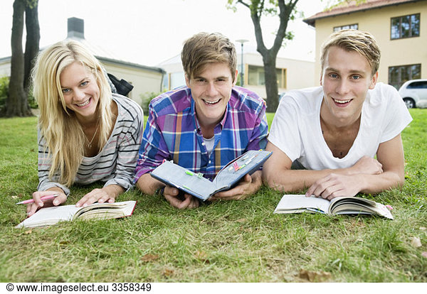 Drei glückliche Schüler liegen draußen und studieren