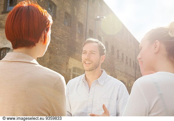 Drei junge Leute im Gespräch  die im Hintergrund bauen