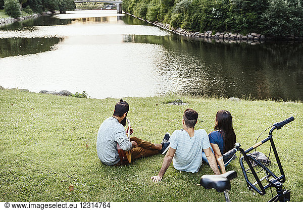 Drei Menschen entspannen im Park mit Gitarre