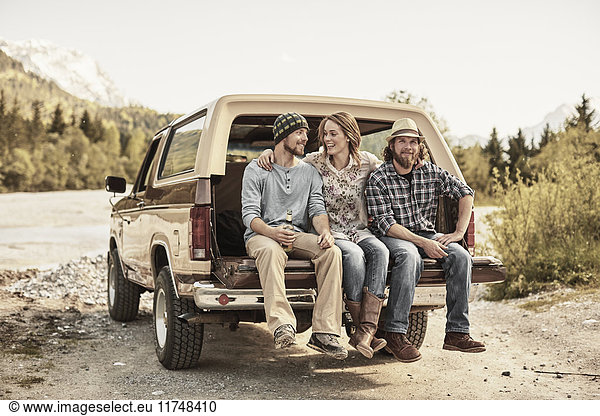 Drei Personen sitzen hinten auf einem Pickup  die Arme um die Schultern gelegt  lächelnd