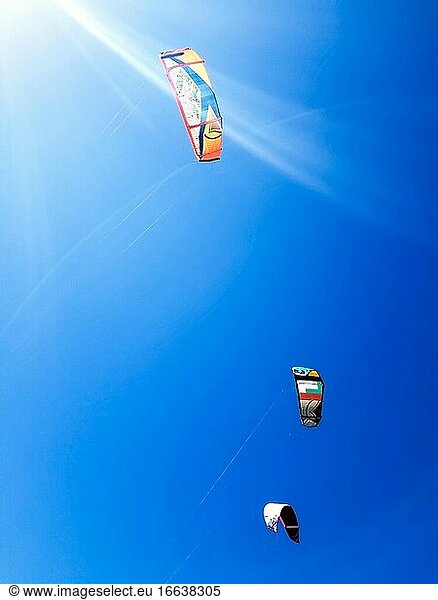 Drei Segel vom Kitesurfen gegen einen blauen Himmel mit Sonnenstrahlen.