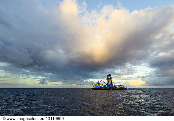 Drill ship in sea against cloudy sky