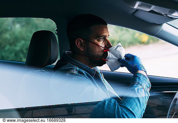Driver adjusting his face mask in the car. Driving with COVID-19.