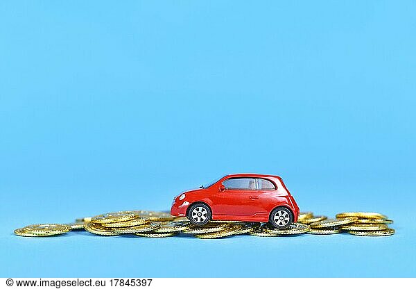 Driving Costs  Small car driving on money coins on blue background with copy space