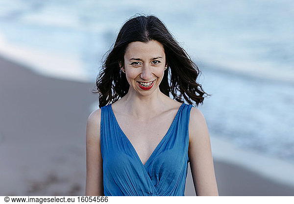 Dunkelhaarige Frau in blauem Kleid am Strand  lächelnd  Porträt