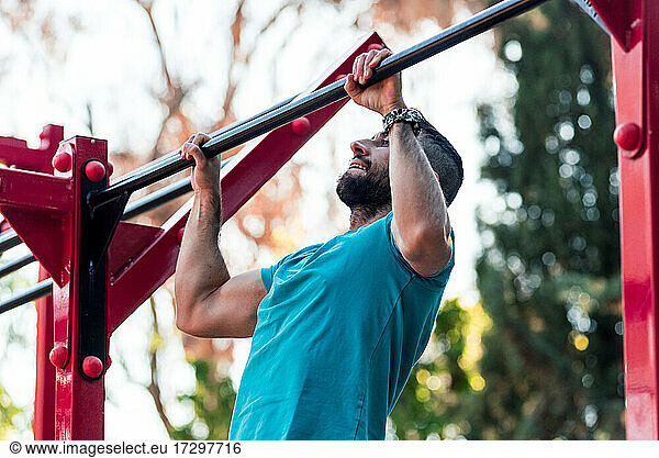 Dunkelhaariger Athlet mit Bart macht einen Klimmzug an einer Calisthenics-Stange. Crossfit-Konzept im Freien.