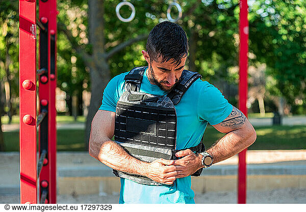 Dunkelhaariger Mann mit Bart passt eine Gewichtsweste in einem Fitnesspark an. Outdoor-Fitness-Konzept.
