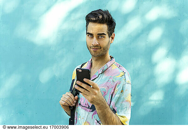 Dunkelhaariger Mann mit Smartphone vor einer blauen Wand