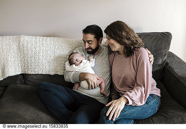 Early-30â€™s parents on sofa lovingly admire newborn baby