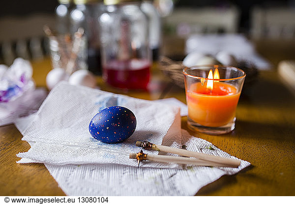 Easter egg with sticks and tissue papers by candle on wooden table