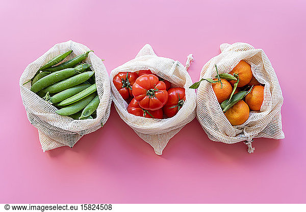 Eco-friendly reusable mesh bags with fresh green peas  tomatoes and clementines