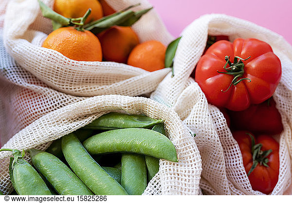 Eco-friendly reusable mesh bags with fresh green peas  tomatoes and clementines