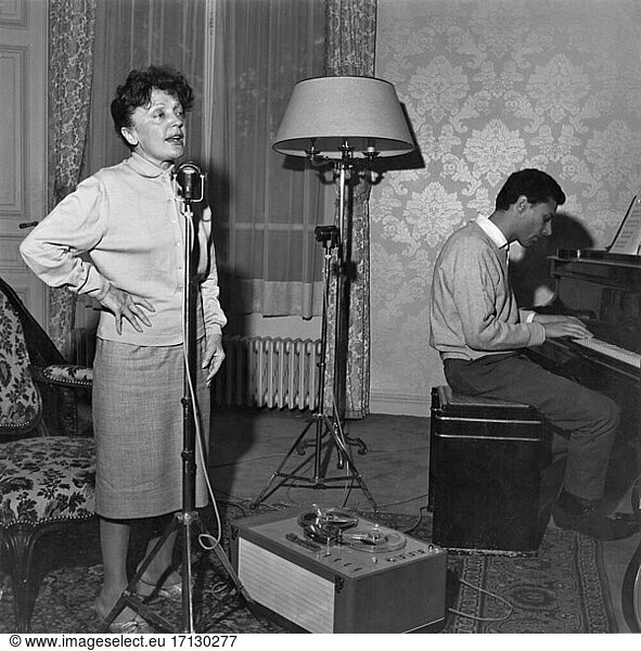 Edith Piaf  (Giovanna Gassion).
French Chansonsängerin  19.12.1915
Belleville – 11.10.1963 Paris. In Piaf’s apartment 67 bis boulevard Lannes  Paris:
She studies the chanson “Milord   while her lover Georges Moustaki accompanies her on the piano (he wrote the chanson text for her in 1959). Photo  end of August / beginning of September 1958.