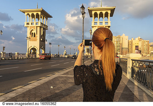 Egypt  Alexandria  Rear view of woman photographing Stanley bridge at sunset