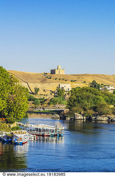 Egypt  Aswan Governorate  Aswan  Tourboats moored on bank of Nile river with Mausoleum of Aga Khan in background