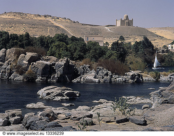 EGYPT Nile Valley Aswan Feluccas on the Nile. View of Felucca sailing among the boulders off Elephantine Island with the Mausoleum of the Aga Khan in the background.