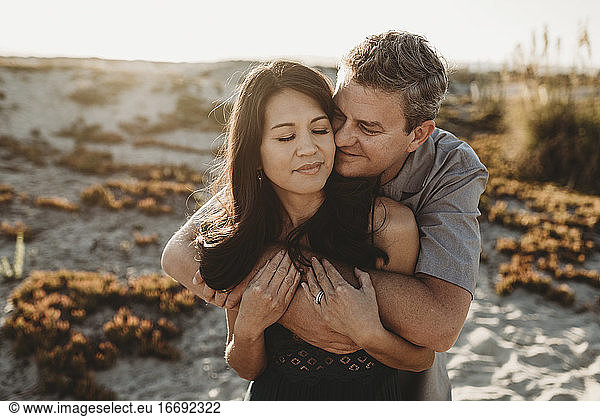 Ehemann Mitte 40 umarmt schöne Frau mit Sanddüne im Hintergrund