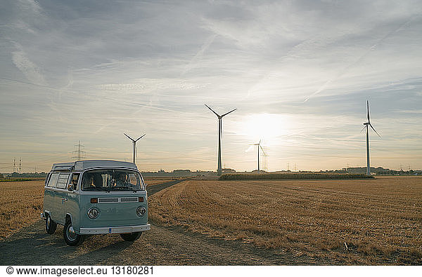 Ehepaar im Wohnmobil in ländlicher Landschaft mit Windturbinen bei Sonnenuntergang