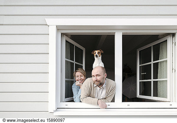 Ehepaar mit Hund lehnt sich aus dem Fenster ihres Hauses