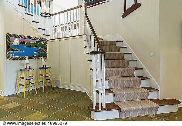 Eichenholztreppe mit weiß gestrichenem Geländer und hellbraunem  gestreiftem Teppichläufer  die in ein modernes Haus in Quebec  Kanada  führt. Dieses Bild ist zur Veröffentlichung in Kalendern und zur redaktionellen Verwendung freigegeben. EUPR0363.