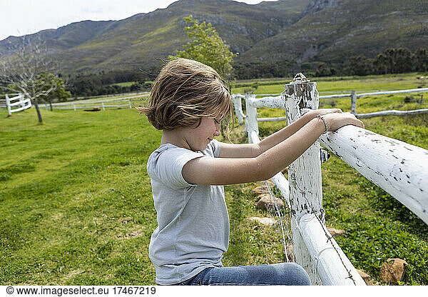 Eight year old boy leaning on a fence  looking at horses in a field