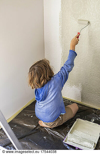 Eight year old boy using paint roller to paint a house wall