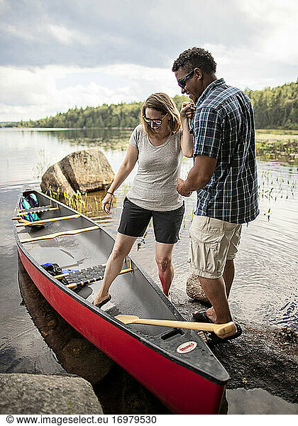 Ein Afroamerikaner hilft einer weißen Frau in ein rotes Kanu auf einem See.