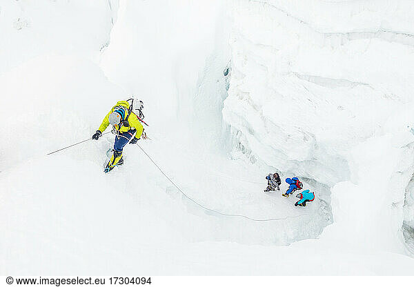 Ein Alpinist seilt sich ab  während das Team unter ihm Gletscherspalten bezwingt