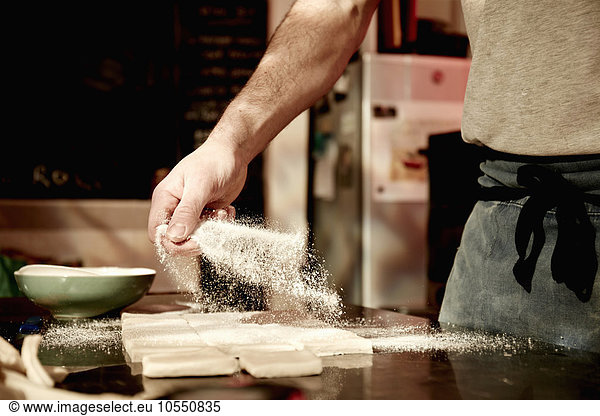 Ein Bäcker  der auf einer bemehlten Oberfläche arbeitet und den vorbereiteten Teig in Quadrate teilt.