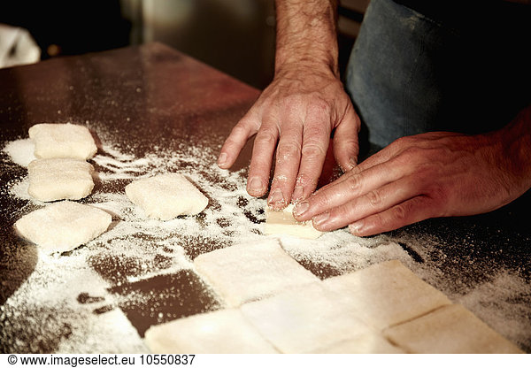 Ein Bäcker  der auf einer bemehlten Oberfläche arbeitet und den vorbereiteten Teig in Quadrate teilt.