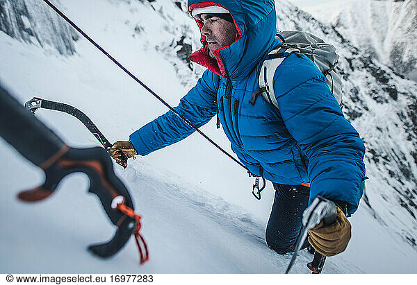 Ein Bergsteiger wird in einem steilen Schneeabschnitt gesichert