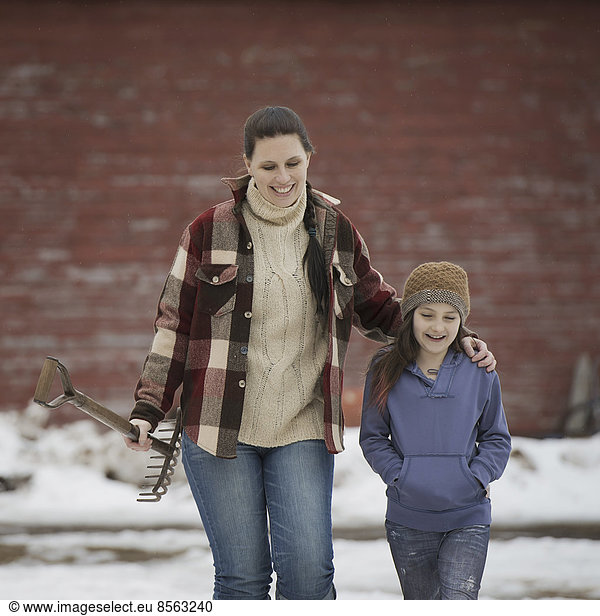 Ein Bio-Bauernhof im Winter im Bundesstaat New York  USA. Eine Frau und ein junges Mädchen gehen über einen schneebedeckten Bauernhof.