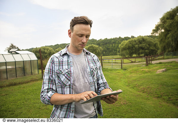 Ein Bio-Bauernhof in den Catskills. Ein Mann mit einem digitalen Tablet in einer Graskoppel.