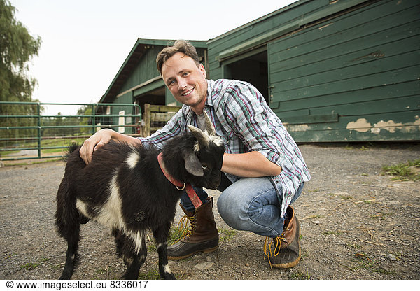 Ein Bio-Bauernhof in den Catskills. Ein Mann mit einer kleinen Ziege an einem Halfter.