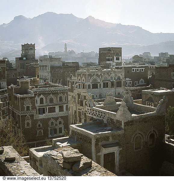 Ein Blick auf die Dächer von San´a. Geometrisch eingeritzter Stuck und kunstvolle Fensterbögen schmücken die Fassaden der mehrstöckigen Häuser. Berge im Hintergrund. Jemen. Islamisch.