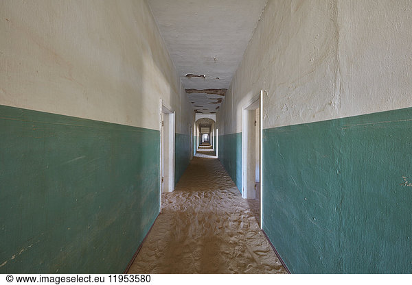 Ein Blick auf einen langen Korridor in einem verlassenen  heruntergekommenen Gebäude voller Sand.