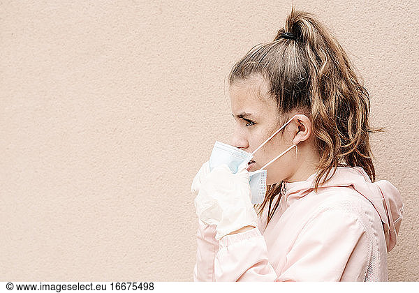Ein blondes Mädchen mit Latexhandschuhen und Gesichtsmaske zeigt  wie sie sich vor Coronaviren  Bakterien  Viren  Pilzen usw. schützt. Sie nimmt die Maske ab  um einen klaren Atem zu bekommen. Horizontal