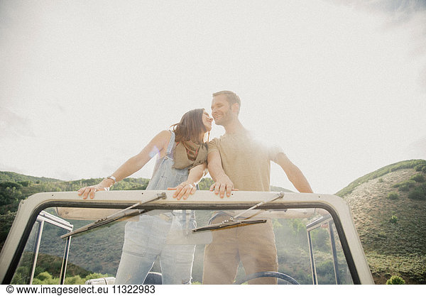 Ein Ehepaar auf einer Autofahrt in den Bergen  die Seite an Seite in einem Jeep stehen und sich umschauen.