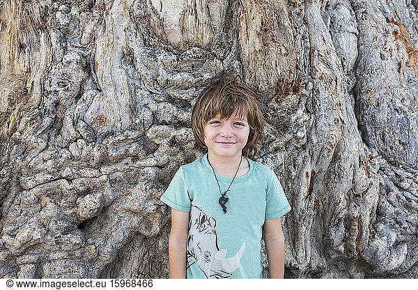 Ein fünfjähriger Junge posiert gegen den Stamm eines großen Affenbrotbaums