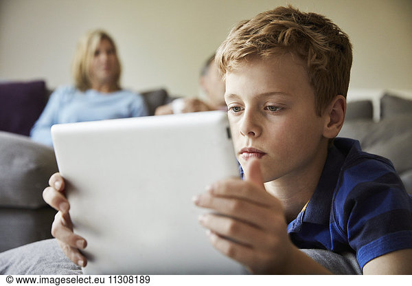 Ein Familienhaus. Ein Junge sieht sich ein digitales Tablet an  das auf dem Boden liegt.