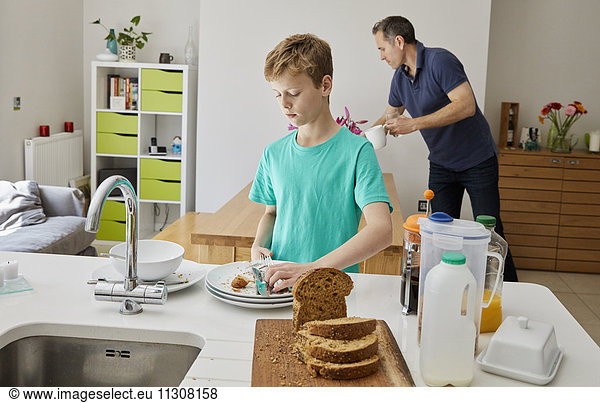 Ein Familienhaus. Ein Mann und ein Junge räumen nach dem Frühstück die Teller ab.