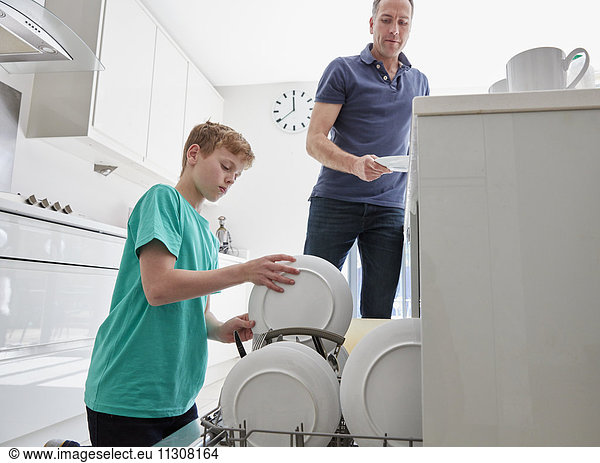 Ein Familienhaus. Ein Mann und ein Junge stellen in einer Küche Teller in den Geschirrspüler.