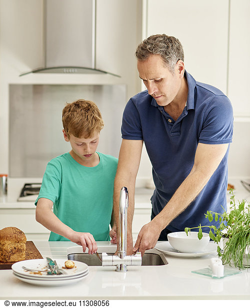 Ein Familienhaus. Ein Mann und ein kleiner Junge nebeneinander in der Küche beim Abwasch.