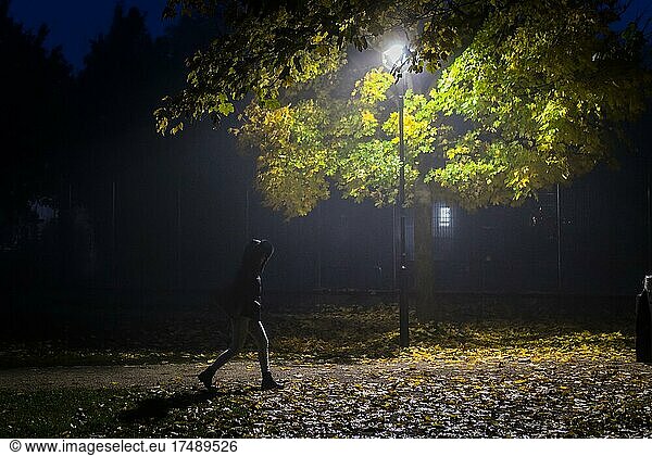 Ein Frau geht an einem dunklen und kalten Herbstmorgen durch eine einsame Parkanlage in Markt Schwaben  Bayern  Deutschland  Europa
