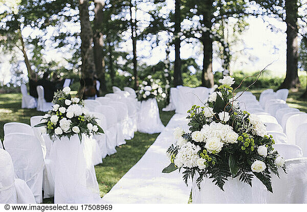 Ein Garten mit Tischen im Schatten hoher Bäume  die für eine Hochzeit gedeckt sind